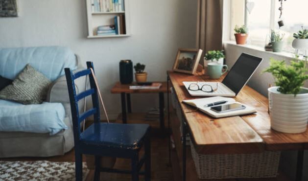 A unoccupied desk with a laptop open which has glasses resting on the keyboard with a pen, notepad, and phone next to it.