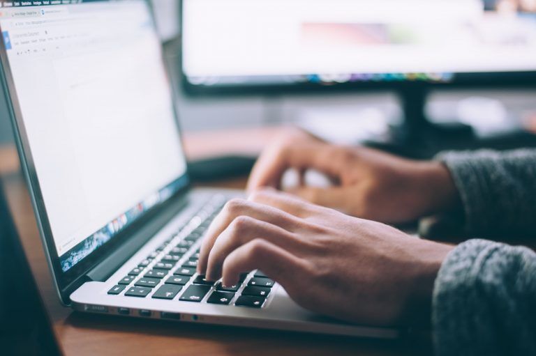 A person typing on a MacBook laptop using Google Docs.