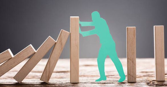 A green cardboard cut out of a person holding a domino block from falling.